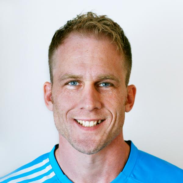 Photo of John Paulsen, CMT. John smiles with blonde short hair and blue shirt with three white stripes on the left shoulder, against white background.