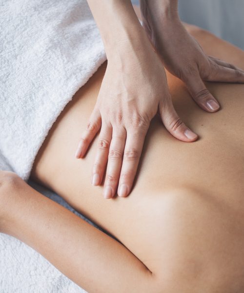 Massage Therapy Image - Back of person lying on massage table, towel covering their lower half. Hands press a massage into their back.