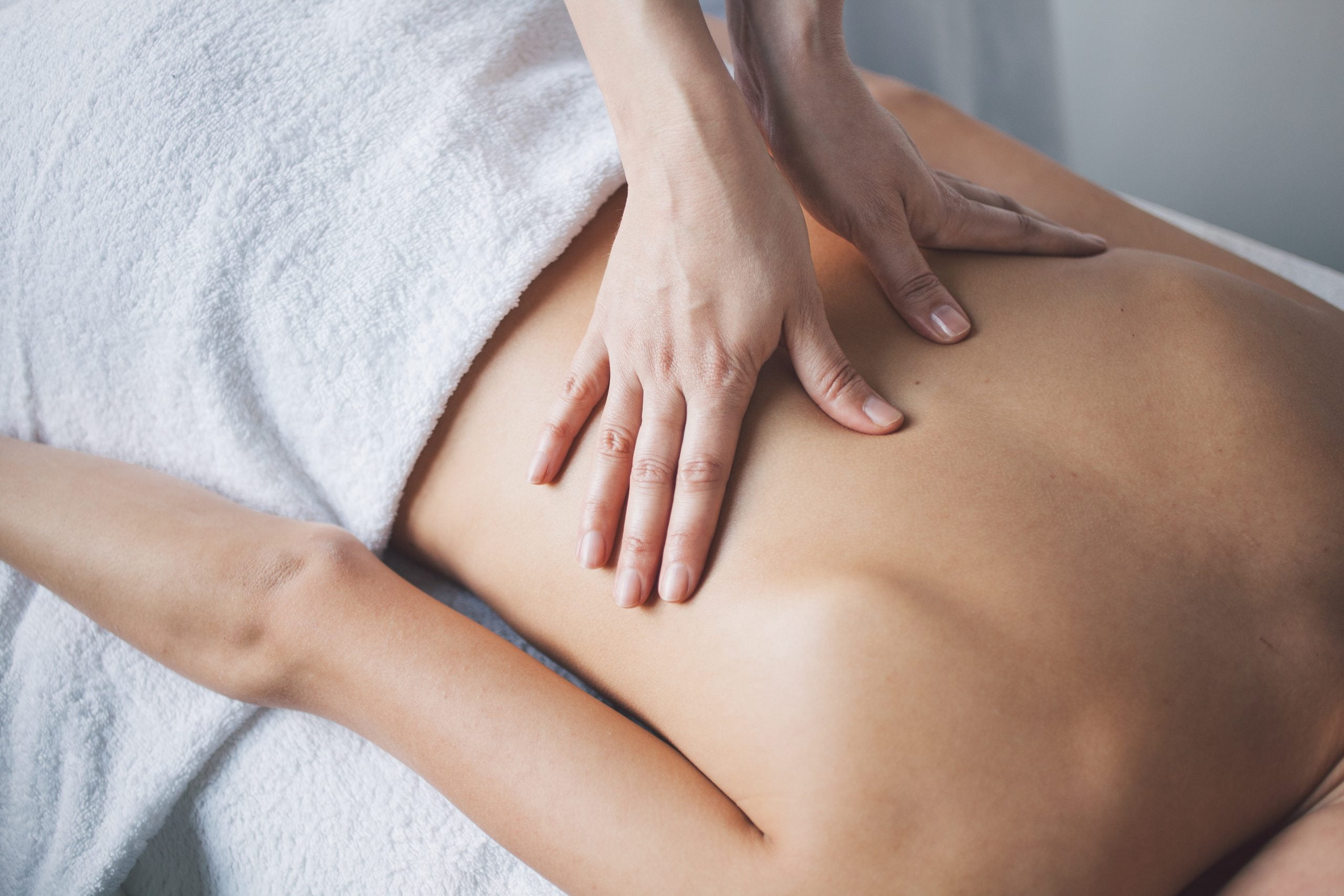 Massage Therapy Massage Therapy Image - Back of person lying on massage table, towel covering their lower half. Hands press a massage into their back.