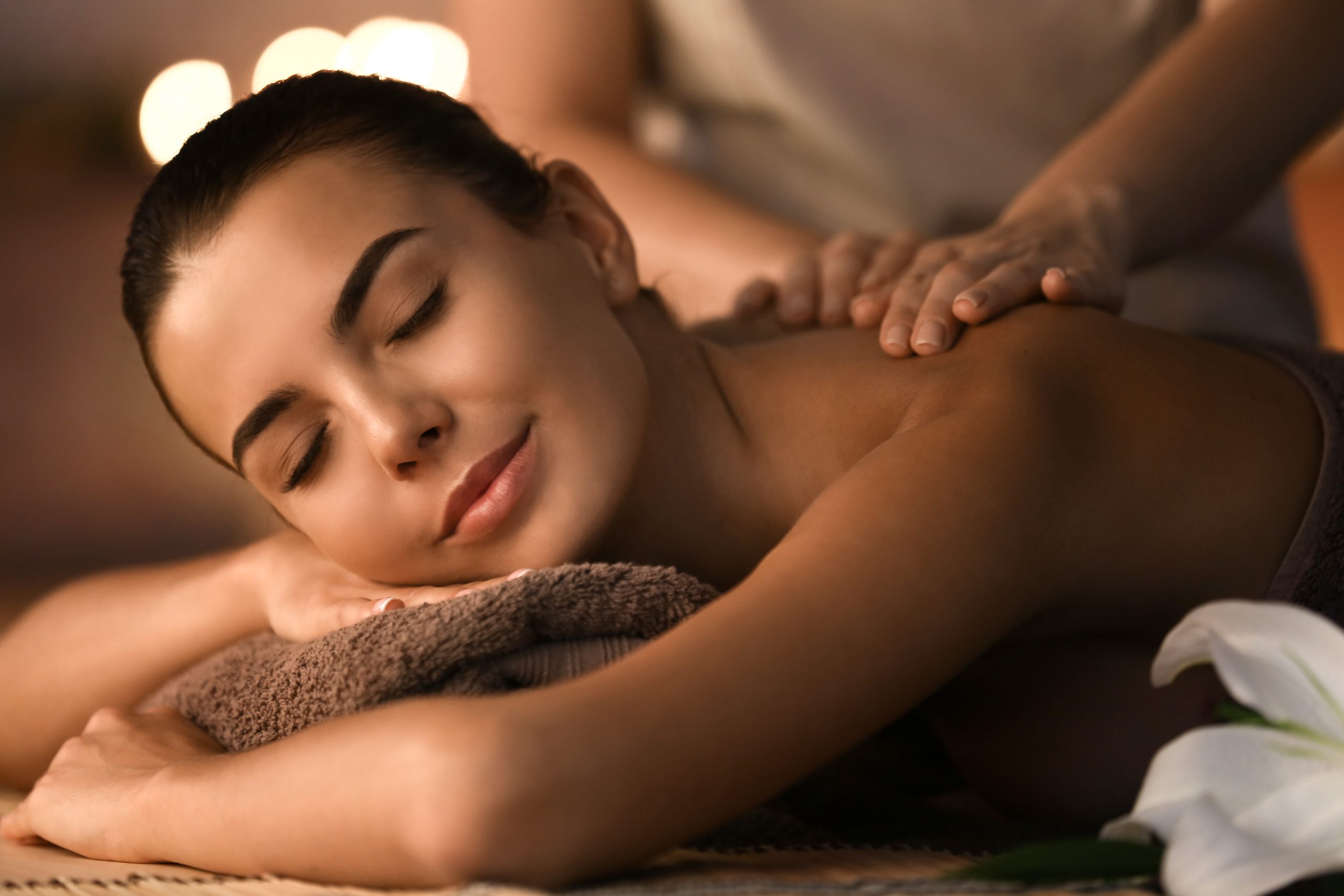 Woman with closed eyes smiling while receiving a relaxing back massage at a spa.