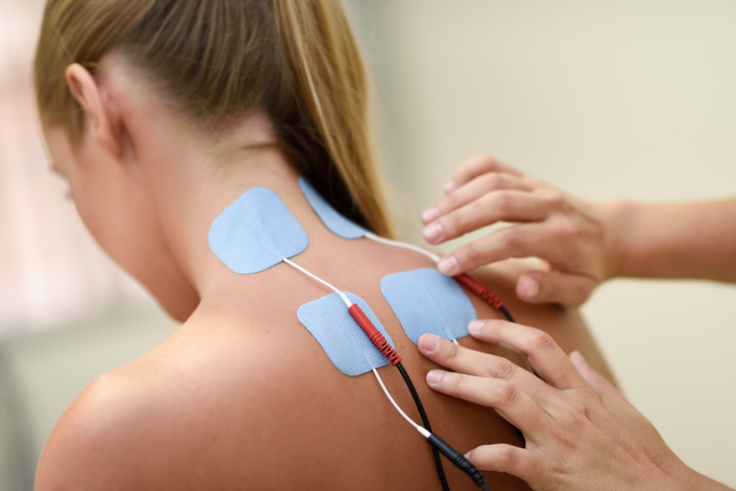 A person has electrode pads placed on their neck and upper back for electrical stimulation therapy.