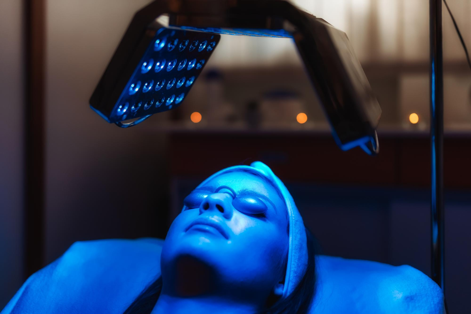 3525 Person lying down with eyes covered, receiving blue LED light therapy treatment on their face.