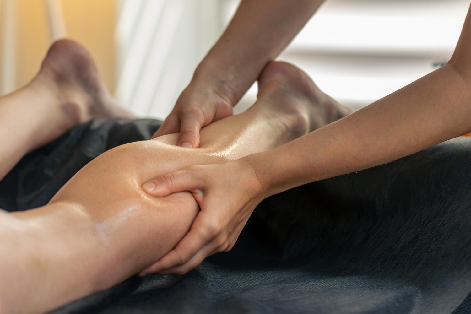 69540 Person receiving a leg massage; hands pressing and massaging an oiled calf on a massage table.